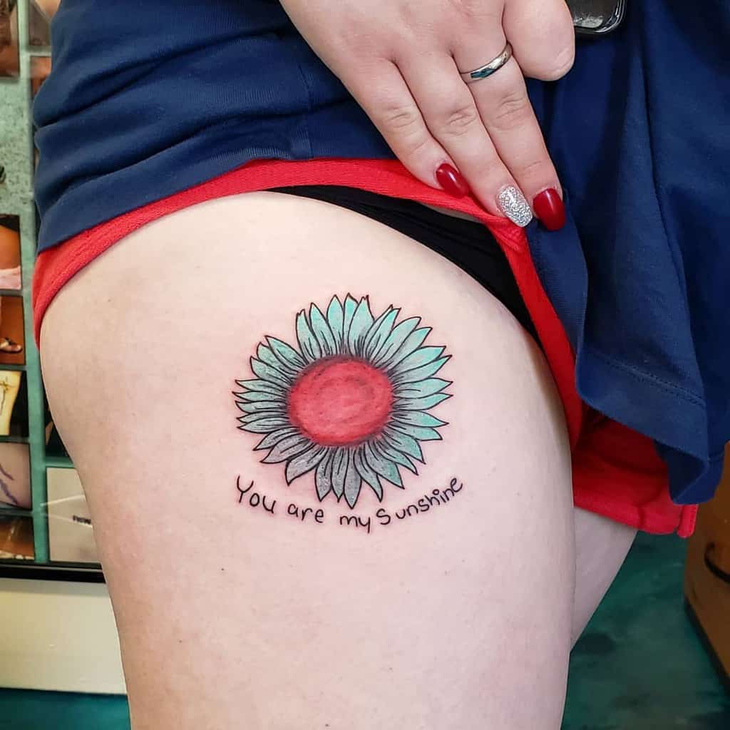 Tattoo of a sunflower with the words "You are my sunshine" on a person's upper leg
