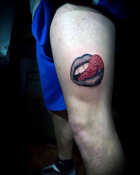 Surreal thigh tattoo of black lips with a textured red tongue resembling a strawberry, blending sensuality with unexpected detail.