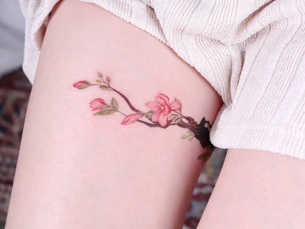 A delicate cherry blossom and magnolia tattoo graces a woman's thigh