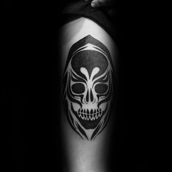 Tribal skull tattoo with hooded figure design, featuring bold black shading and symmetrical white linework for a mysterious, grim look.