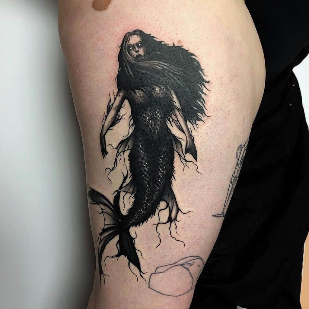 Black and grey tattoo of a haunting, ghostly mermaid with glowing eyes, jagged fins, and eerie flowing hair, designed in a dark art style.