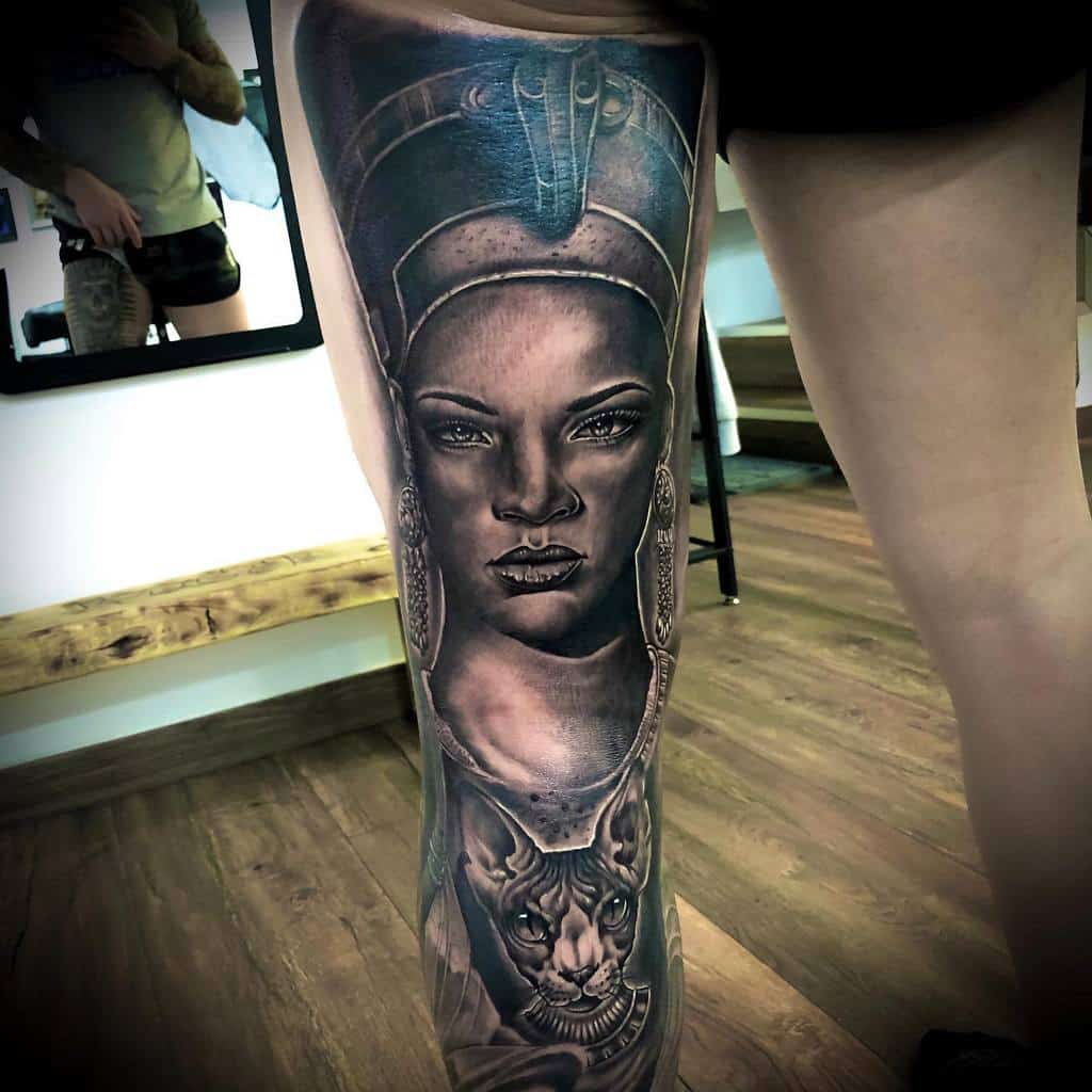Realistic Rihanna as Nefertiti thigh tattoo, featuring intricate shading and a regal Bastet depiction for a divine aesthetic