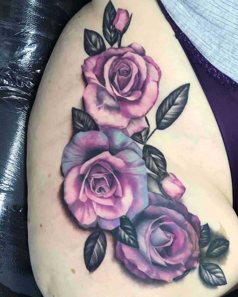 A stunning tattoo featuring a purple rose, accompanied by lush leaves, elegantly adorns the arm