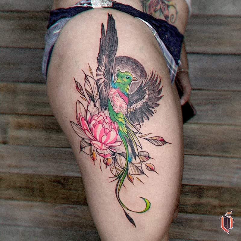 Elegant quetzal tattoo on the thigh, featuring a vibrant green and red bird in flight with black wings, surrounded by detailed pink flowers and a moon-like background