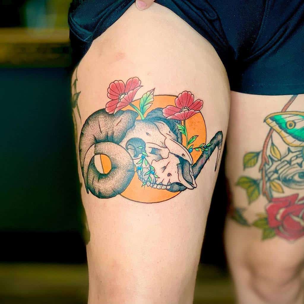 Tattoo of a ram skull surrounded by flowers and leaves on a person's thigh