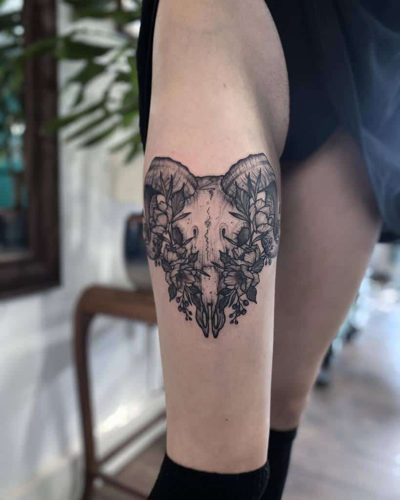 A leg tattoo featuring a ram skull intricately entwined with detailed leaf designs