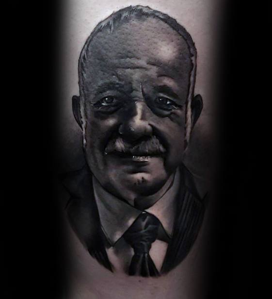 Realistic black and gray tattoo of a man's face, showing detailed shading and texture