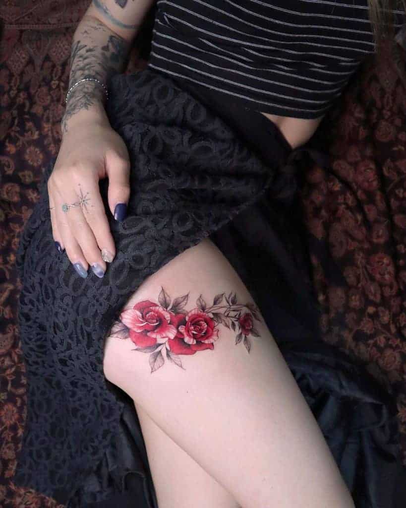 Thigh tattoo featuring vibrant red roses with detailed leaves, arranged in an elegant floral design