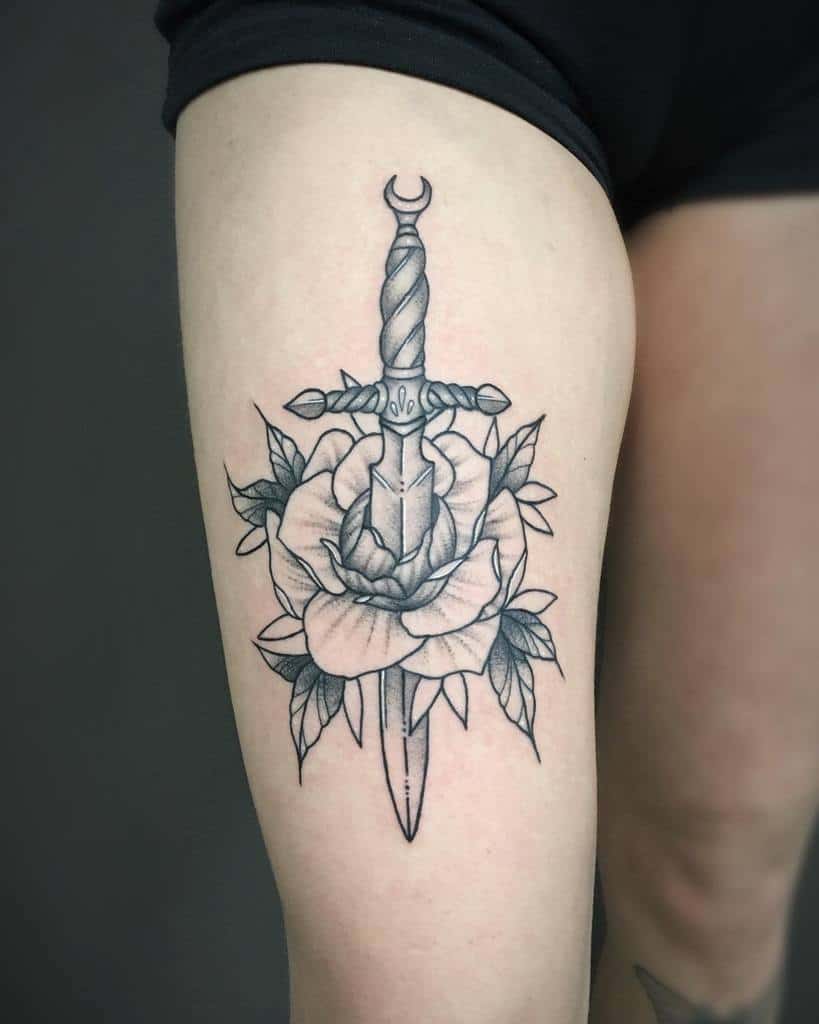 Traditional tattoo of a dagger piercing a rose with leaves on a thigh