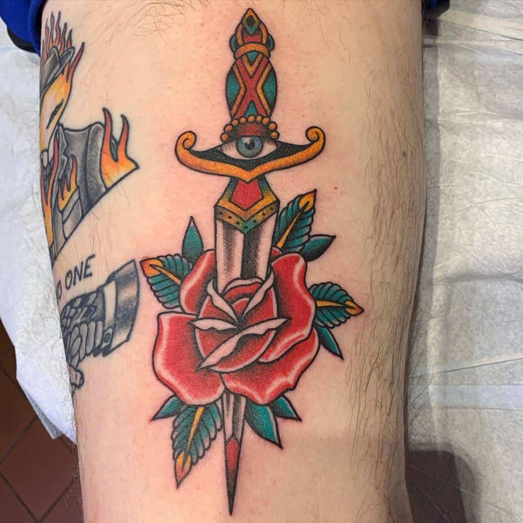 An American traditional tattoo of a dagger through a red rose with leaves on an arm