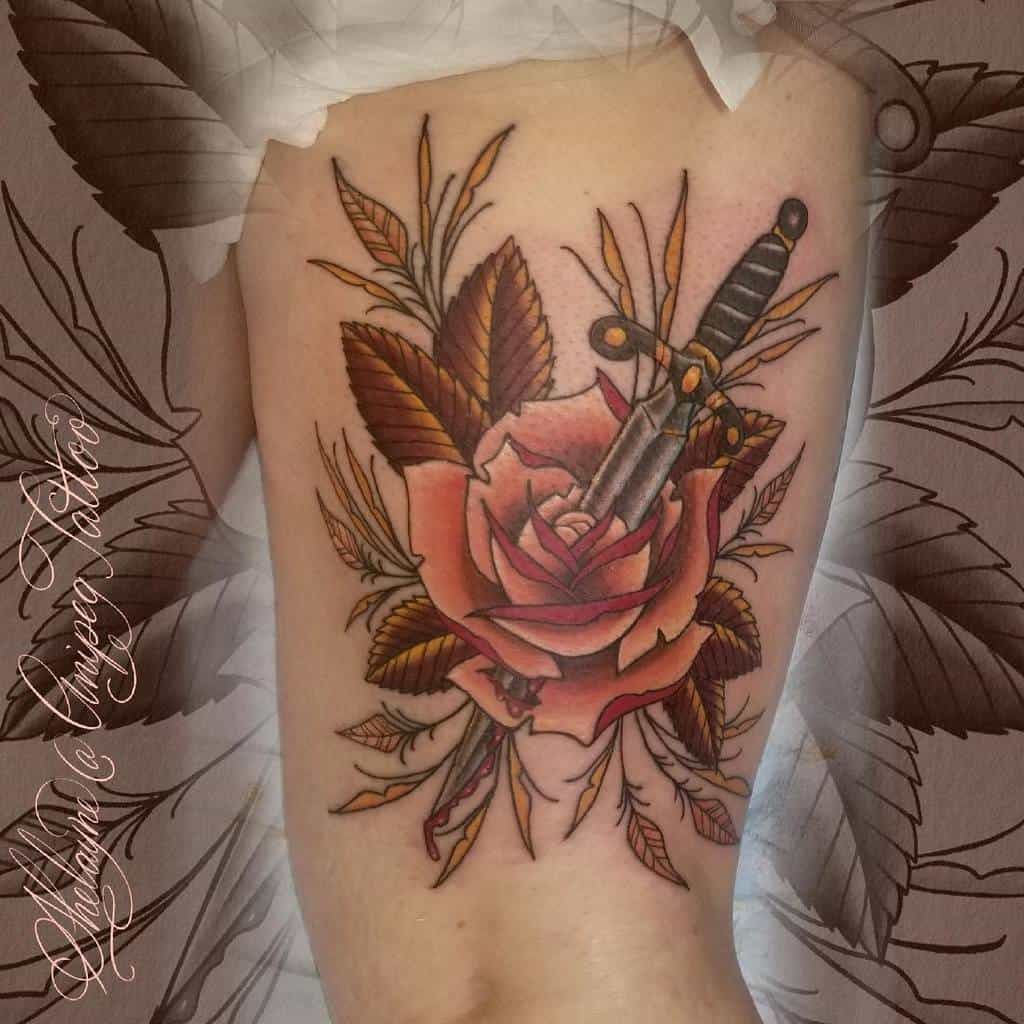 Tattoo of a dagger through a rose with leaves on skin