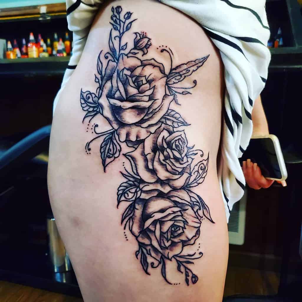 This intricate thigh tattoo showcases a trio of blooming roses intertwined with delicate vines and leaves, creating a bold and elegant design