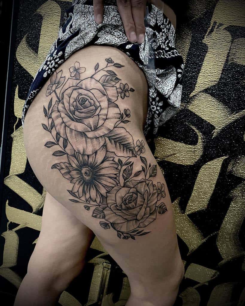 This stunning thigh tattoo blends detailed roses and daisies with a mix of delicate vines and leaves, showcasing a harmonious black-and-grey design