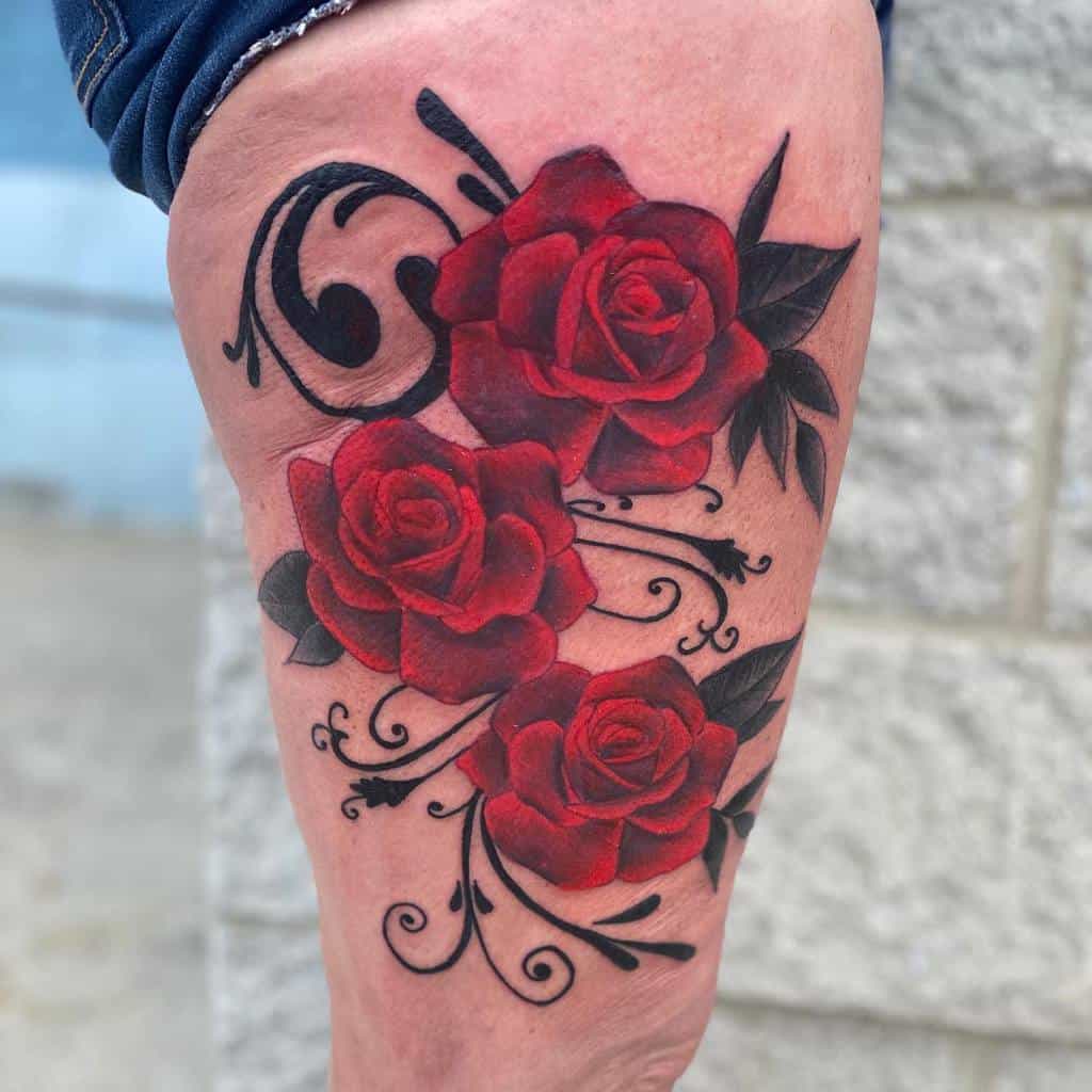 Tattoo of three red roses with black swirls and leaves on a thigh