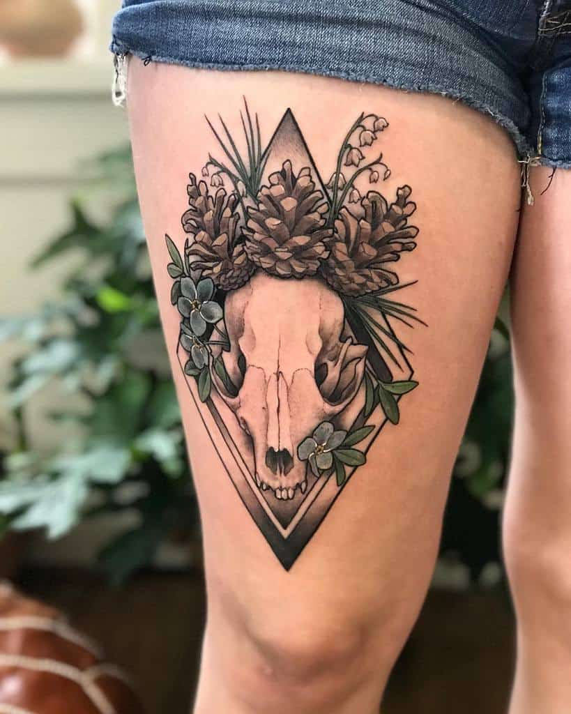 Tattoo featuring a detailed animal skull framed by pinecones, Lily of the Valley flowers, and geometric elements