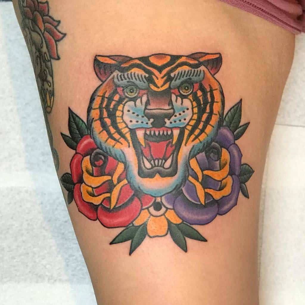 Colorful tattoo of a tiger's head with red and purple roses on a thigh