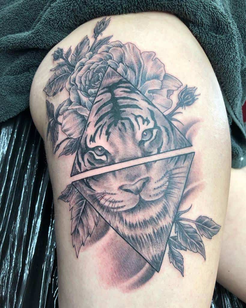 Tattoo of a tiger's face framed by geometric shapes and surrounded by flowers on a thigh