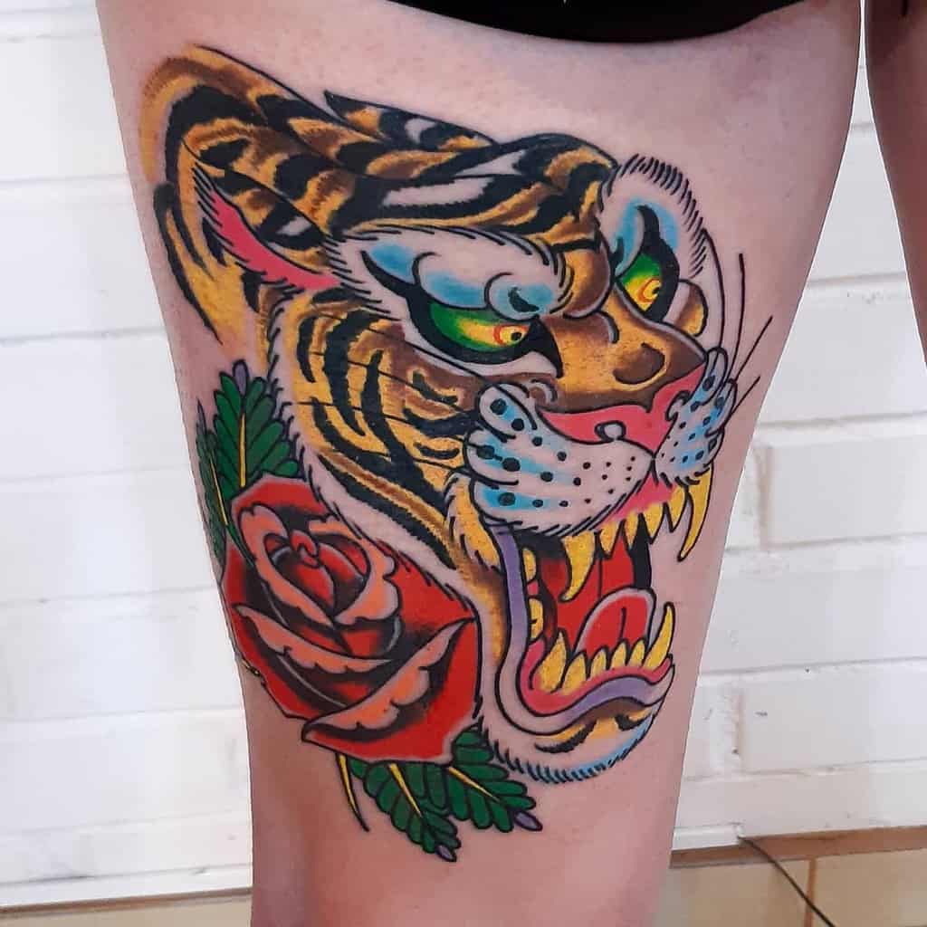 Colorful tattoo of a tiger head and a rose on a thigh