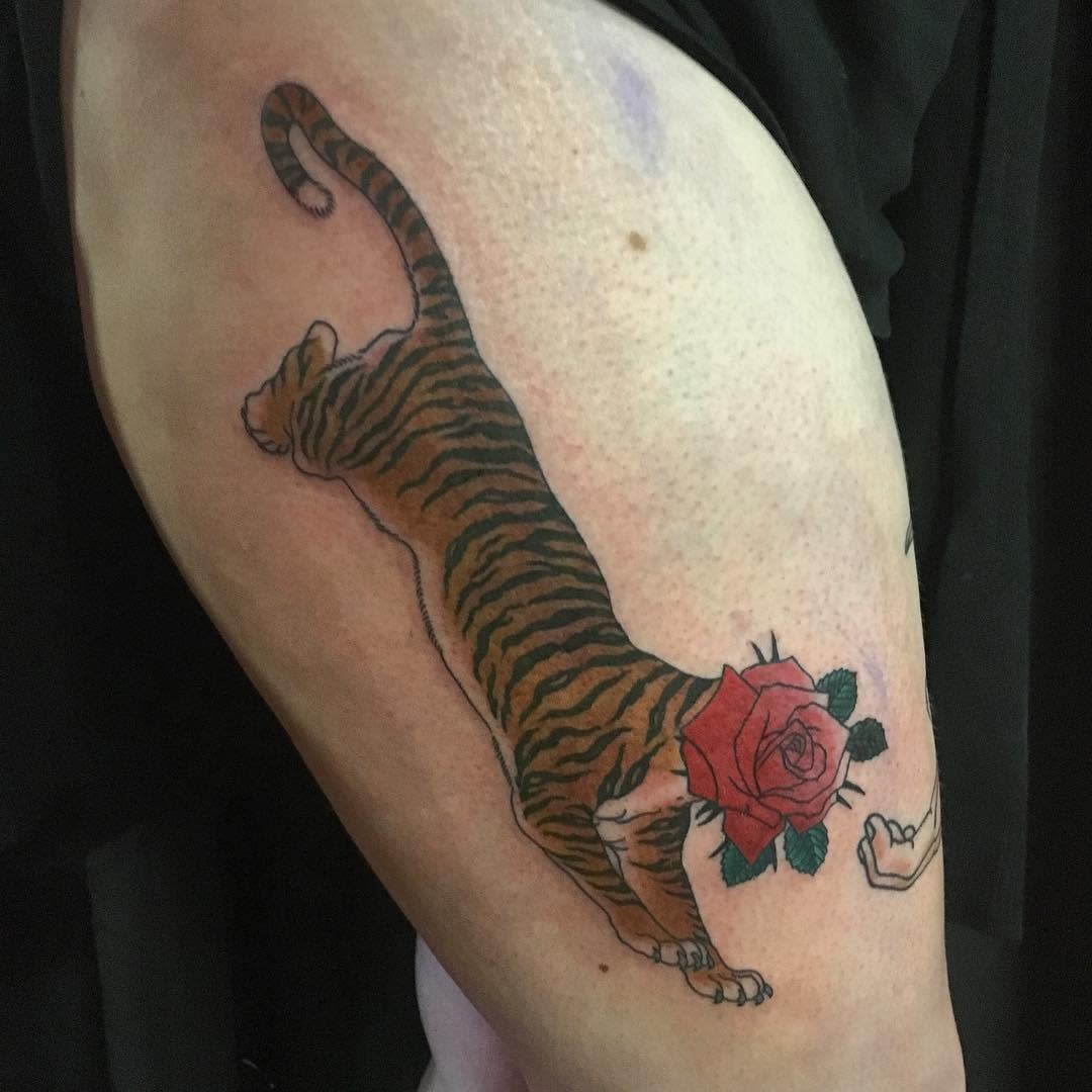 A striking tattoo of a tiger, its fierce body seamlessly merging into a delicate rose where the head should be, graces the person's arm