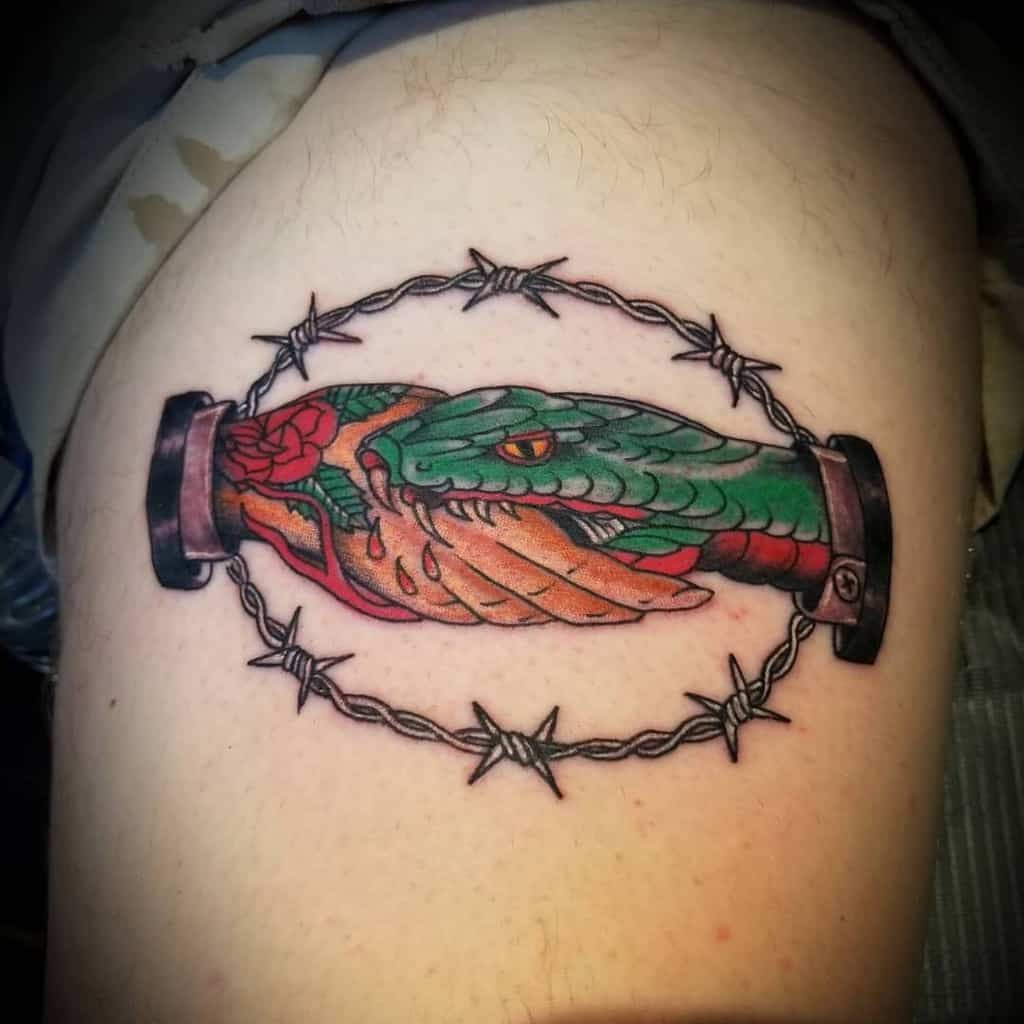 Bold thigh tattoo featuring a snake and handshake wrapped in barbed wire, with vibrant colors and striking details