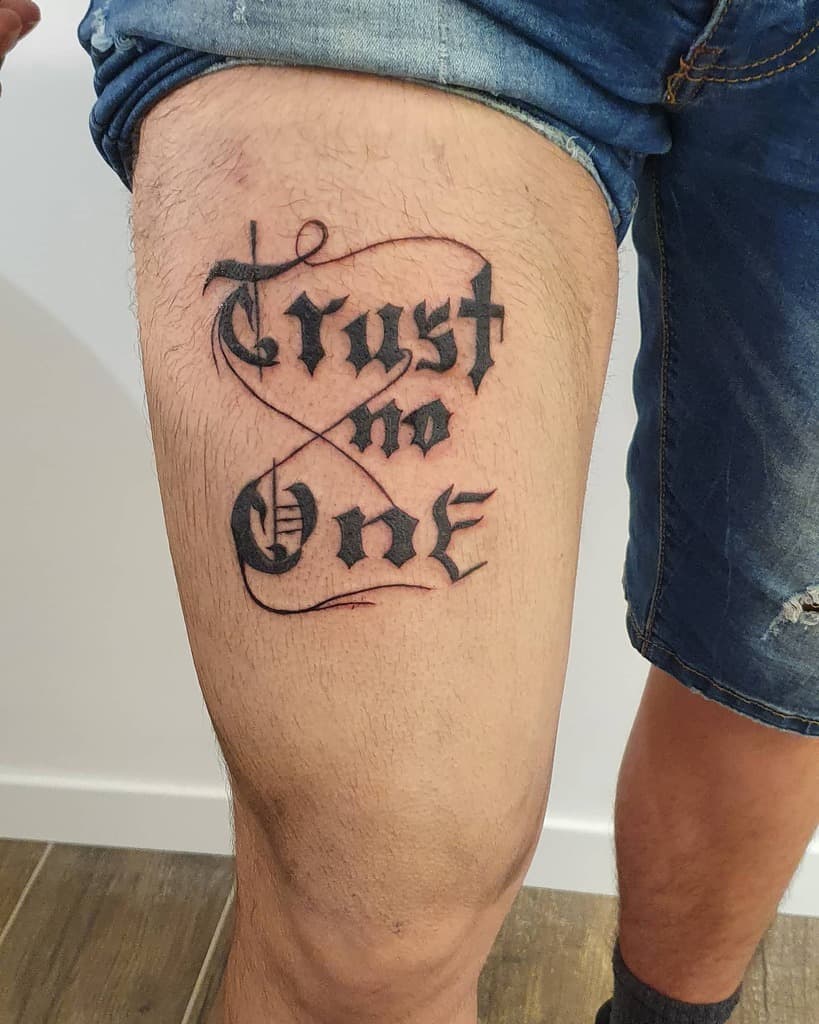 Tattoo on a thigh reads "Trust no one" in stylized black lettering