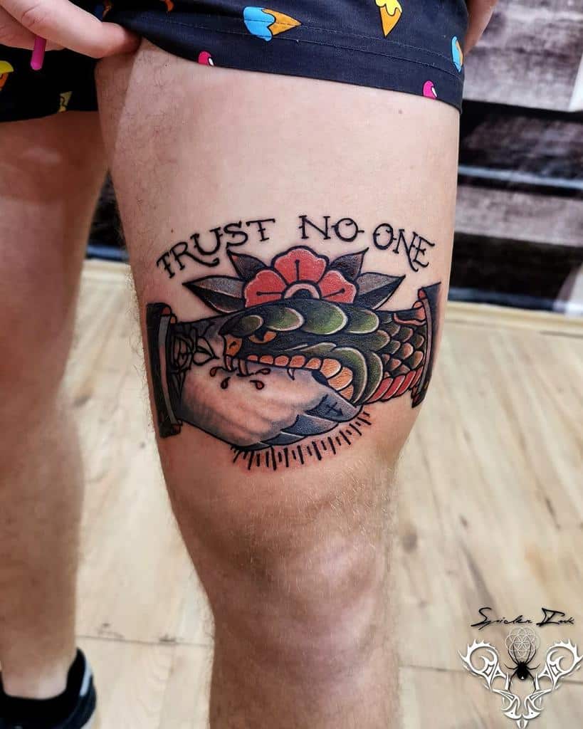 Thigh tattoo of a snake wrapped around a hand, with a flower and "Trust No One" text