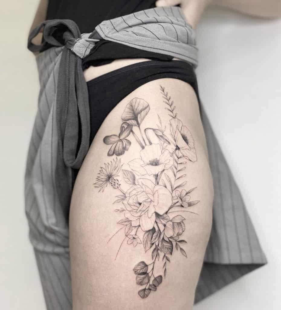 Elegant thigh tattoo featuring a detailed arrangement of wildflowers, leaves, and mushrooms in fine black ink with soft shading
