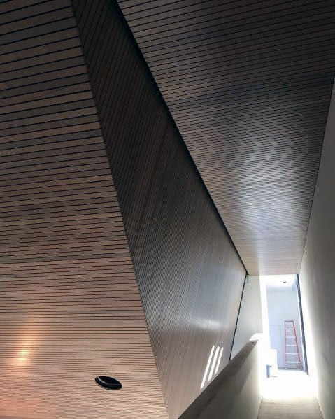 Modern hallway with slatted wood plank ceiling and walls, featuring sleek linear design.