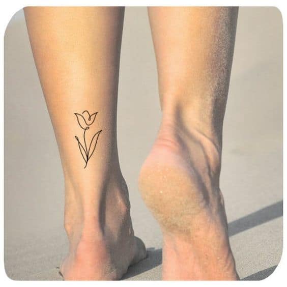 A simple black-line tulip tattoo on the calf, featuring a delicate flower with a slender stem and two leaves.