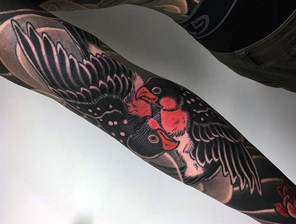 Tattoo of two detailed birds with red accents and wings spread, inked on a person's arm