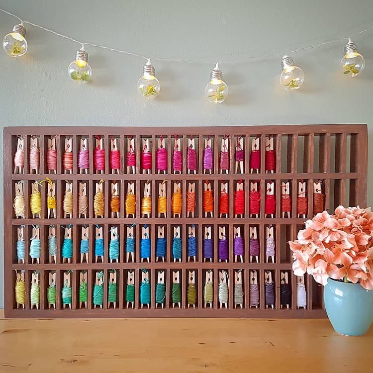 Colorful thread spools arranged in a wooden rack, with decorative string lights and pink flowers in a vase