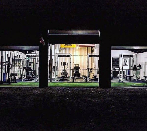 Three-car garage gym at night with power racks, cardio equipment, and turf flooring.