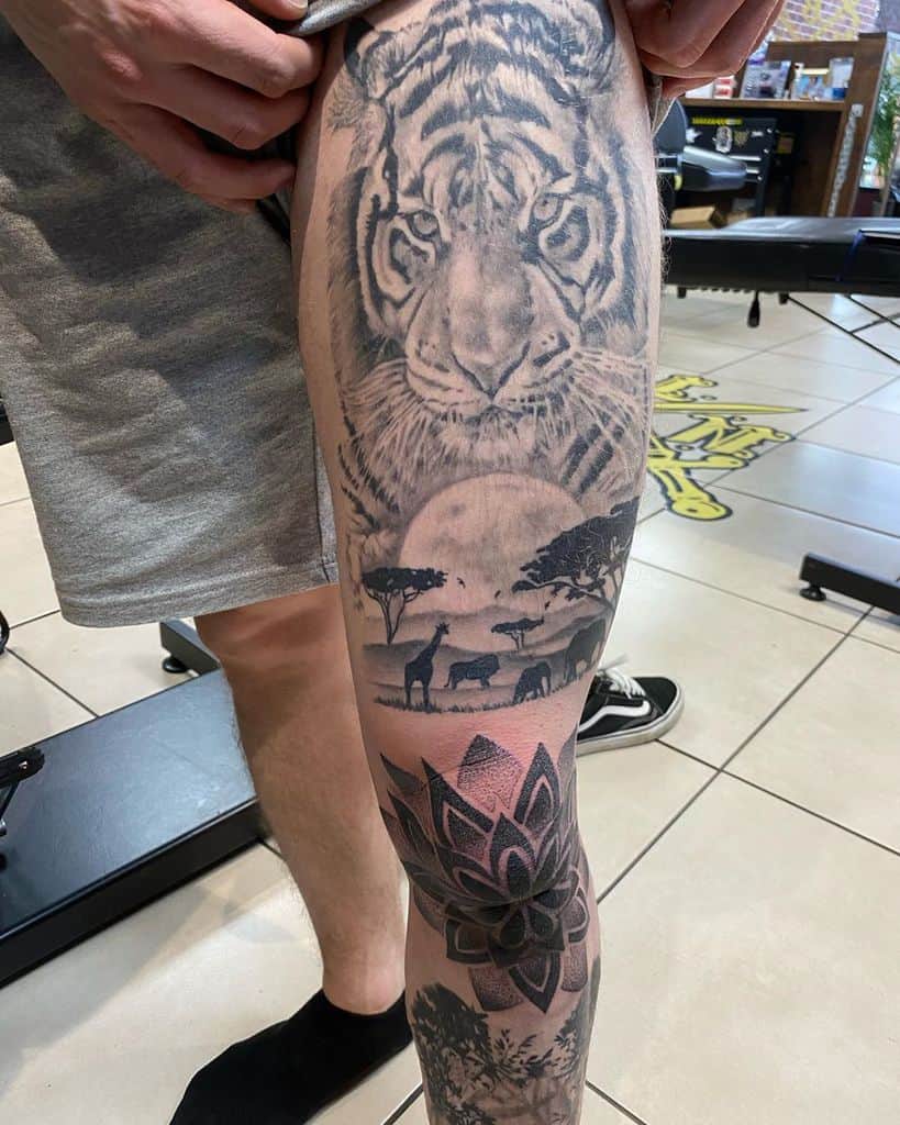 Leg sleeve tattoo featuring a tiger, savannah landscape with trees and animals, and abstract flower geometric design with trees below it