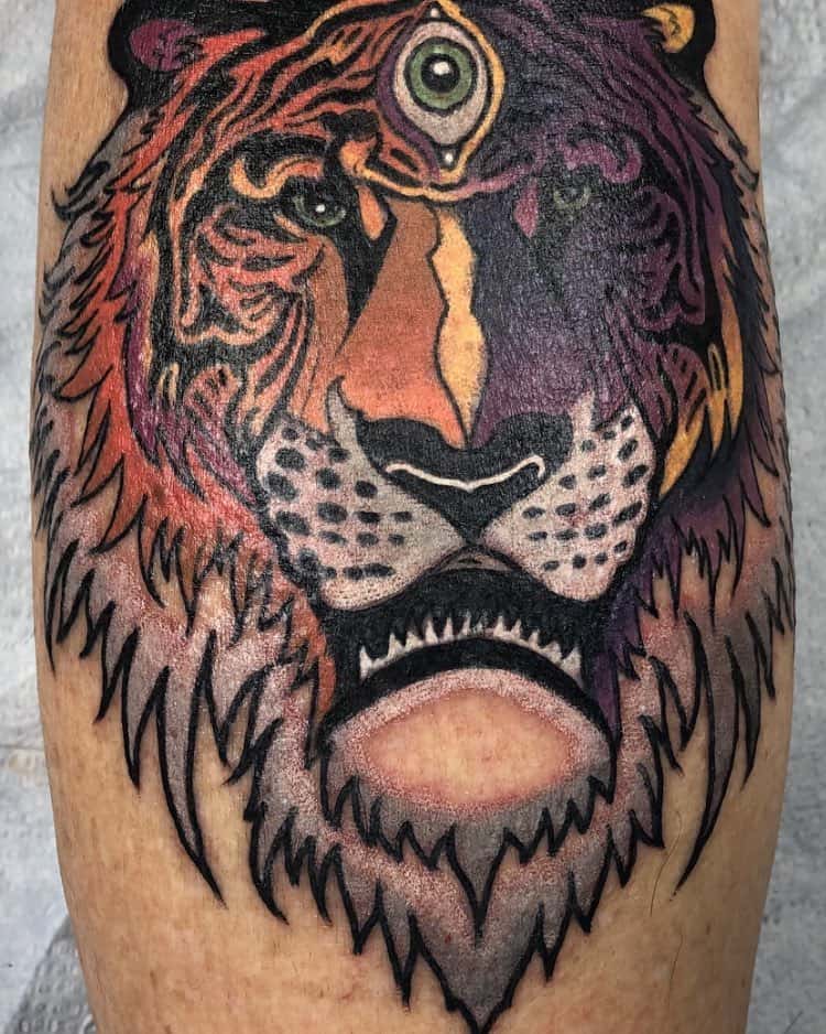 Tattoo of a fierce tiger with a third eye on its forehead, inked in bold black outlines with orange and purple shading.