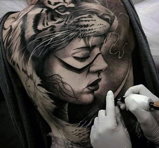 Tattoo artist working on a detailed tattoo of a woman's profile and a tiger on someone's back