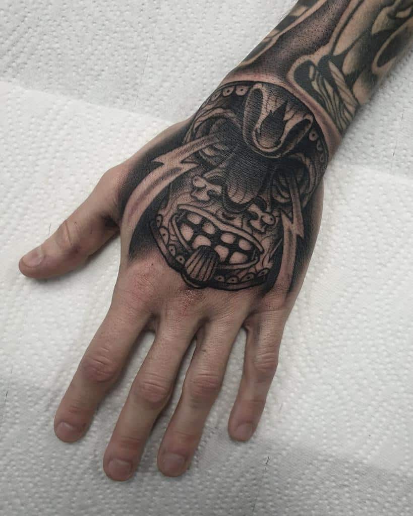 A detailed black-and-gray tattoo of a Tiki mask, featuring sharp facial features and intricate designs