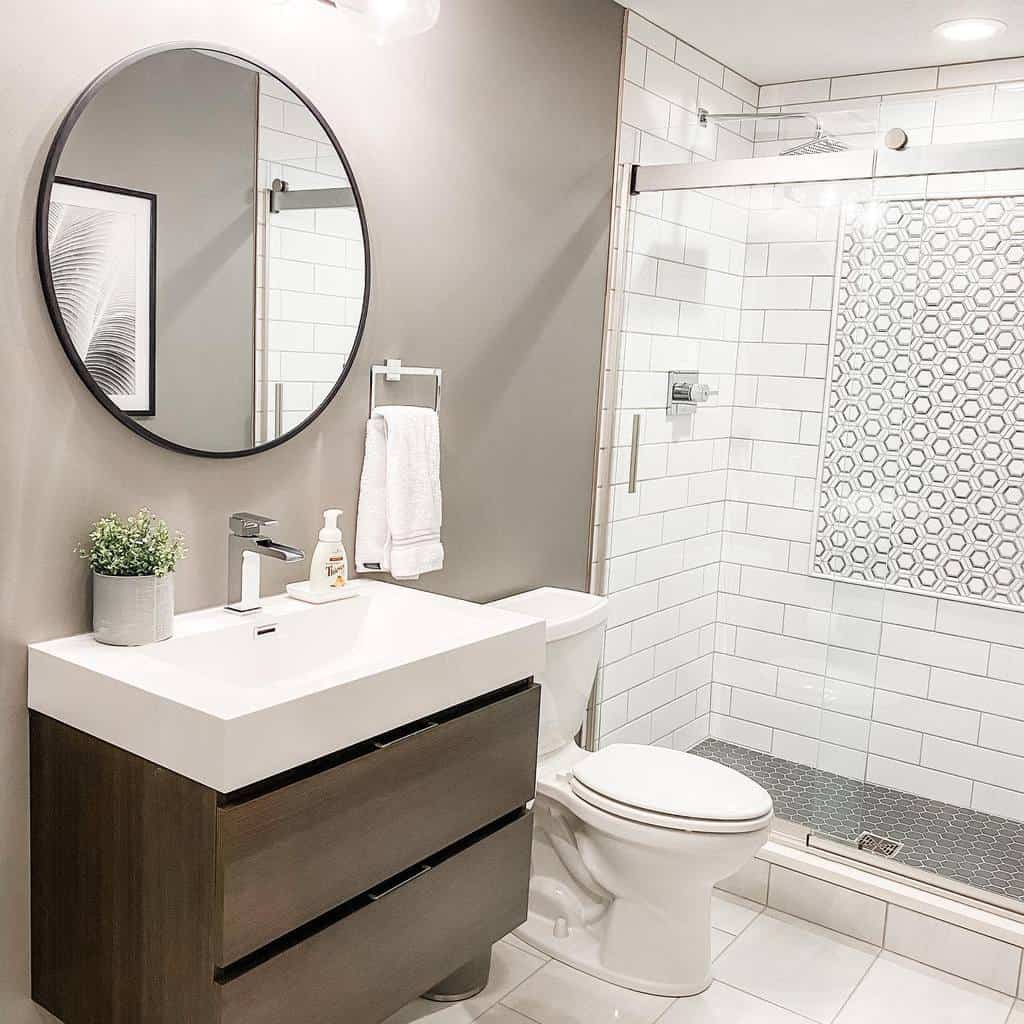 Modern bathroom with round mirror, subway tile shower, and brown vanity with white sink.