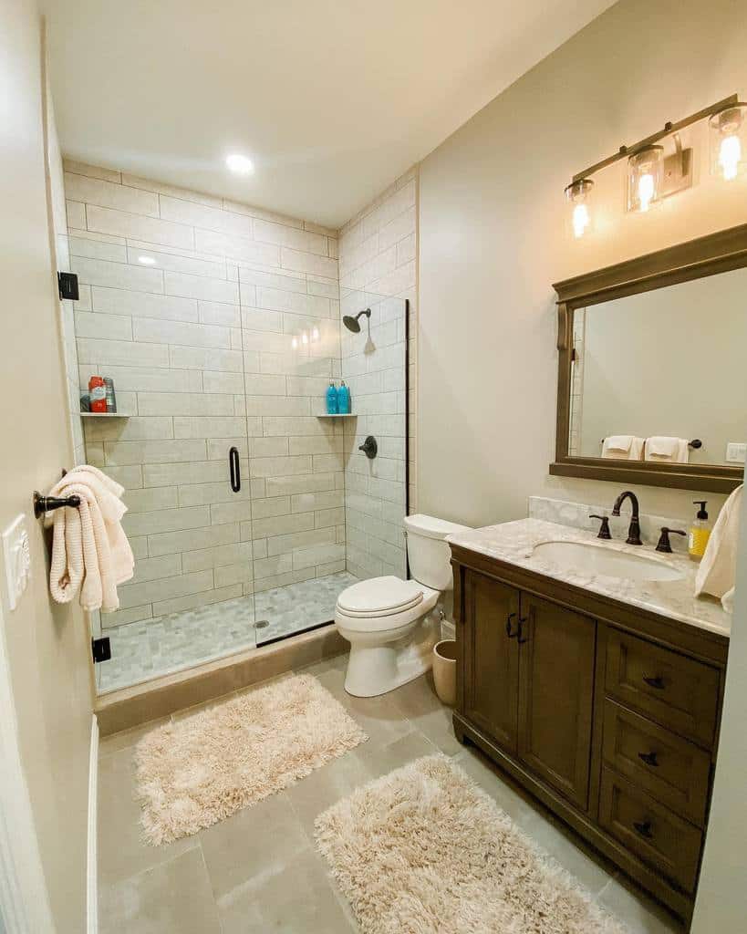 Rustic bathroom with glass shower, wooden vanity, and soft beige rugs.