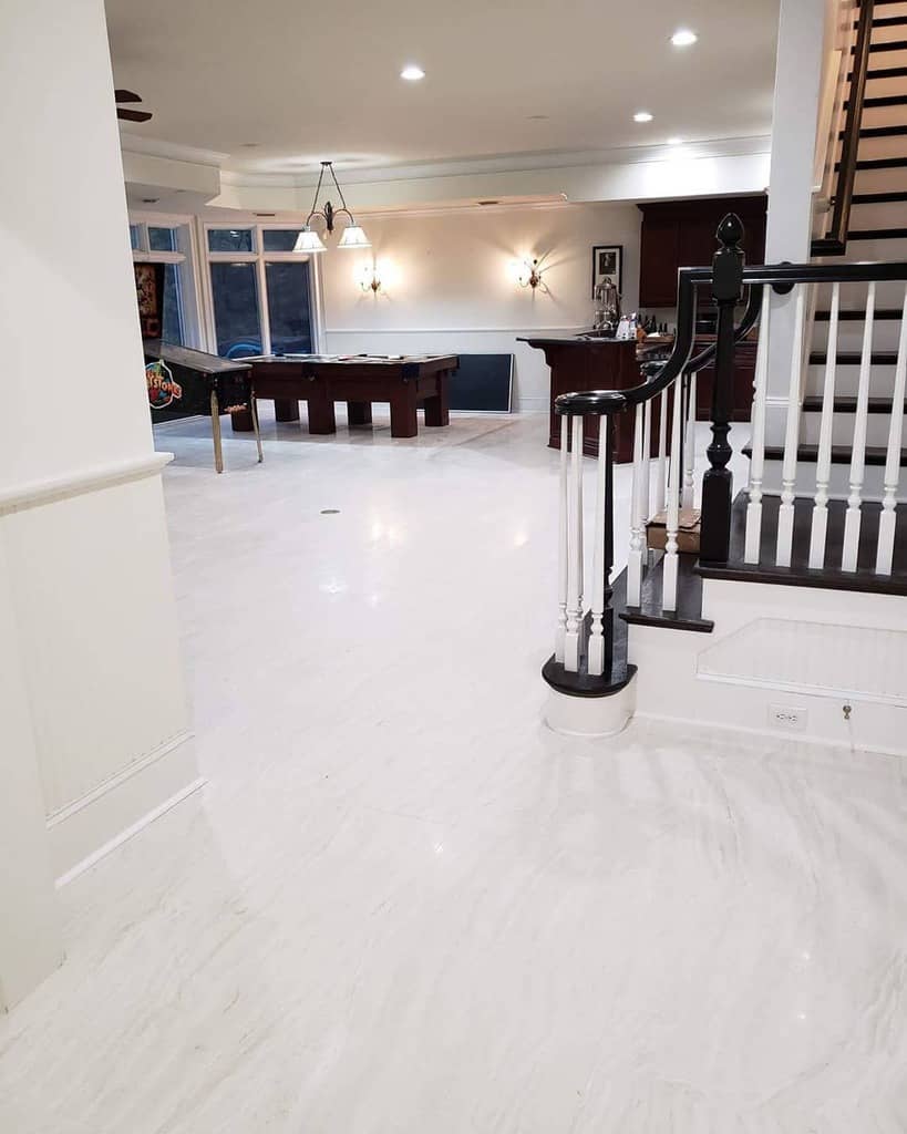 Spacious game room with white marble flooring, pool table, and elegant staircase.