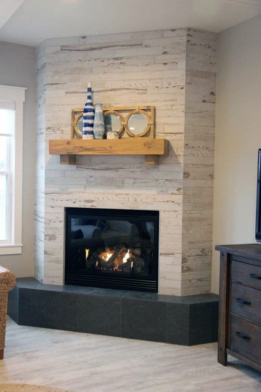 Cozy corner fireplace with whitewashed wood tile surround, wooden mantel, and black stone hearth.