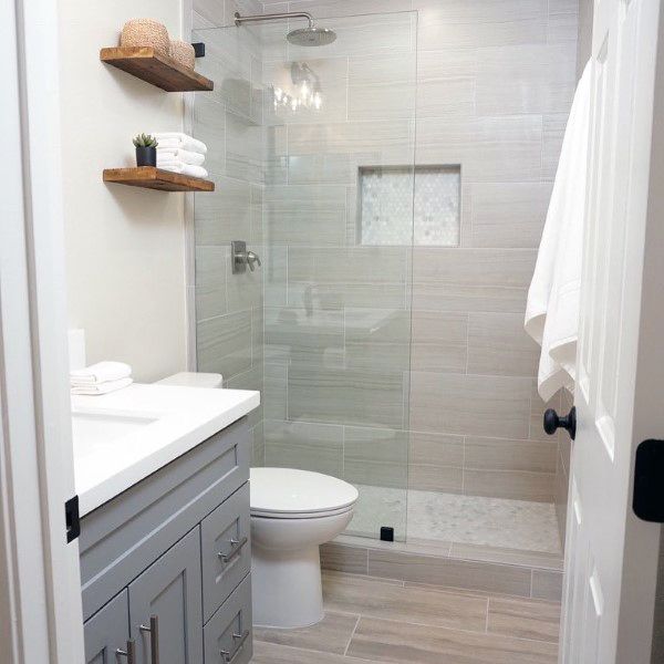 Glossy porcelain tile shower with built-in niche and modern vanity in a small bathroom.