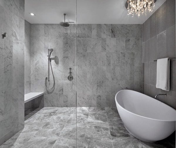 Modern bathroom with gray marble tiles, freestanding tub, walk-in shower, and crystal chandelier.