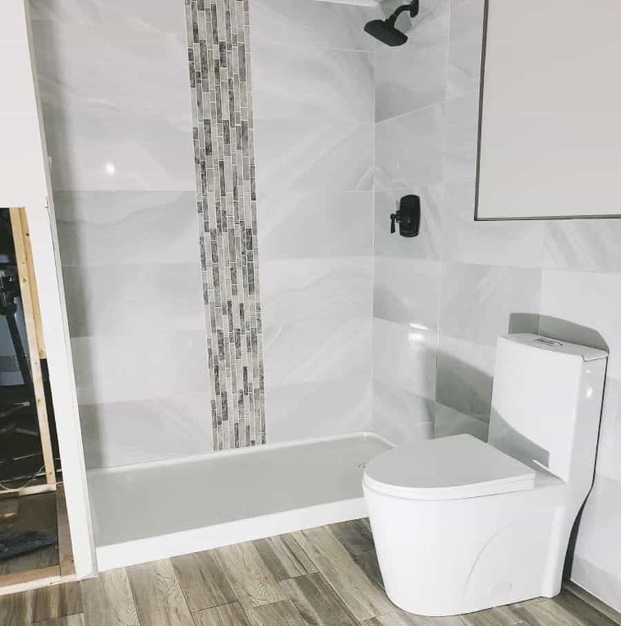 Contemporary bathroom with vertical accent tiles in shower, modern toilet, and wood-look flooring.
