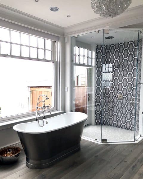 Modern bathroom with black freestanding tub, glass shower, and patterned tile walls.