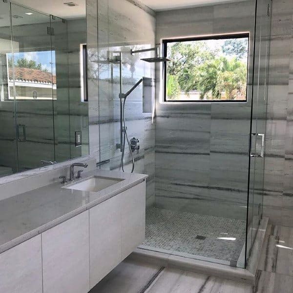 Modern travertine tile shower with glass enclosure, rainfall showerhead, and natural light.