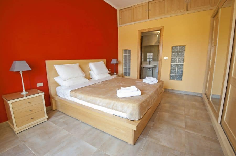 Neutral bedroom with red feature wall, tiled floors, and light wood furniture.