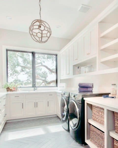 Bright laundry room with white cabinets, black appliances, large window, and woven storage baskets.