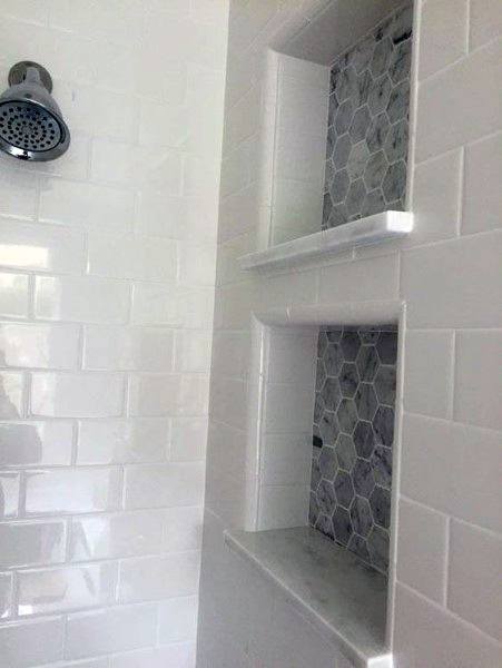 White beveled subway tile shower with hexagonal tile niches and chrome showerhead.