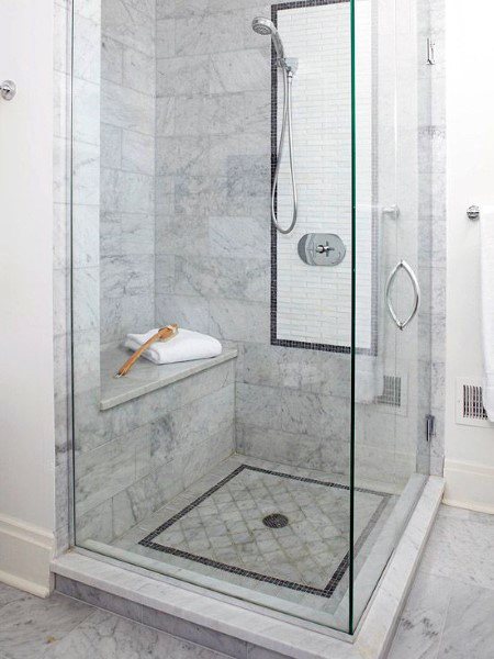 Small marble shower with built-in bench, handheld showerhead, and decorative floor tile border.