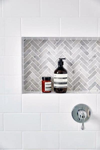White subway tile shower with grey herringbone patterned niche and chrome fixtures.